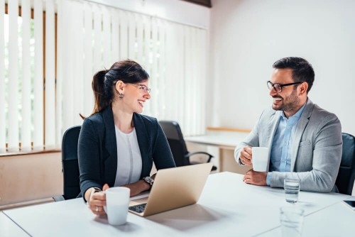 two-smiling-business-people-drinking-tea-coffee-while-sitting-office-deskcedf6587b94e63e5.jpg